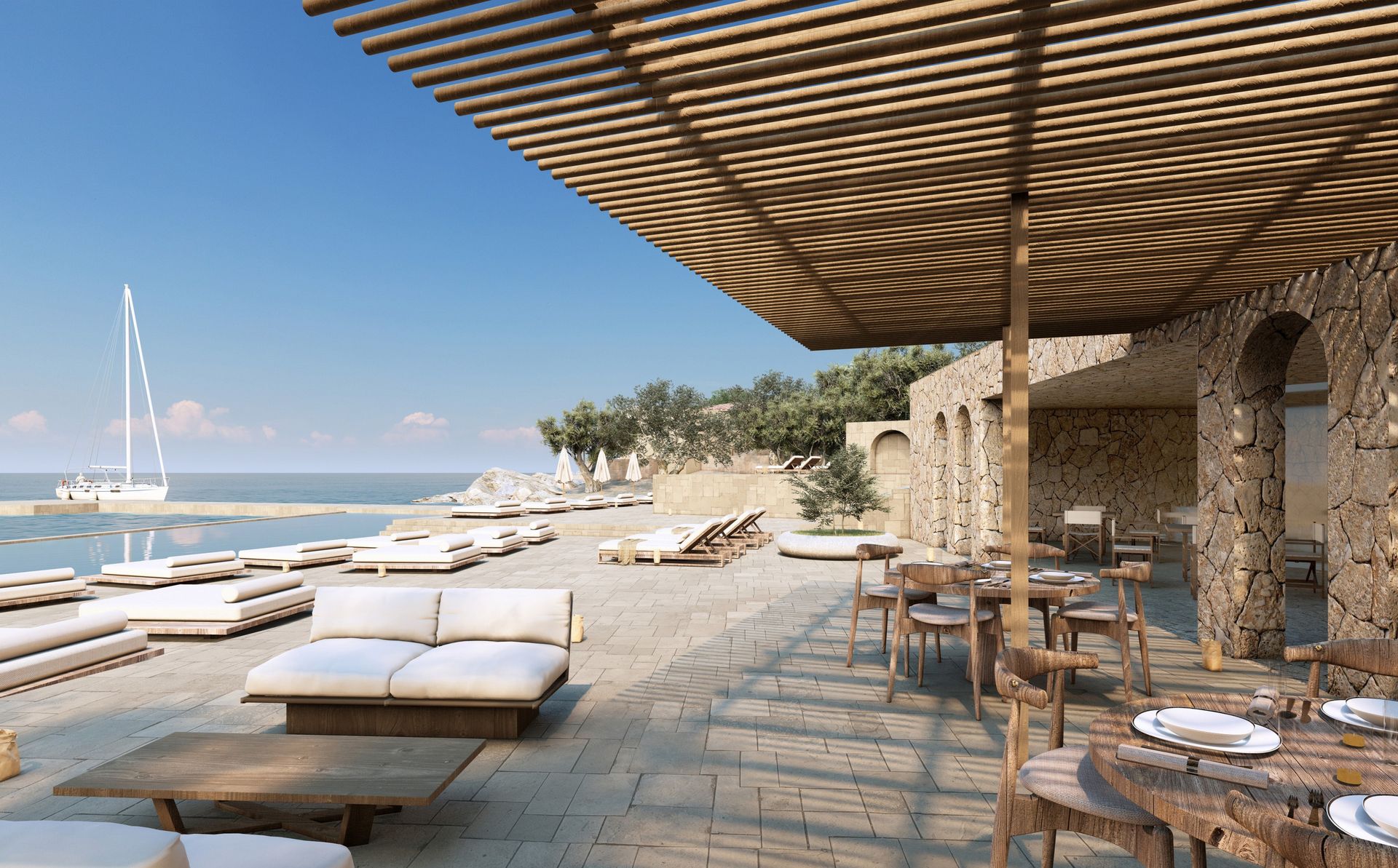 Dining deck of the village beach club with daybeds, a stone arcade and a sailing boat offshore
